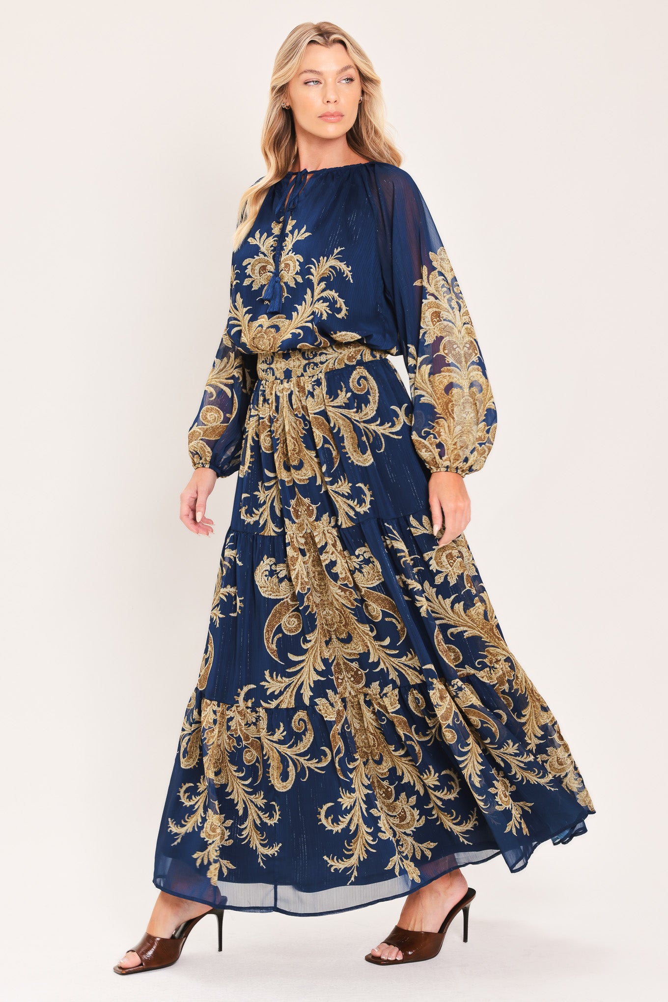 A woman wearing a navy blue long-sleeve blouse with an ornate gold baroque-style pattern and a tie-neck detail | Flying Tomato