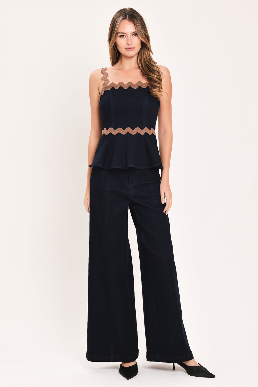 A woman wearing a navy blue sleeveless peplum top with brown wavy trim details | Flying Tomato