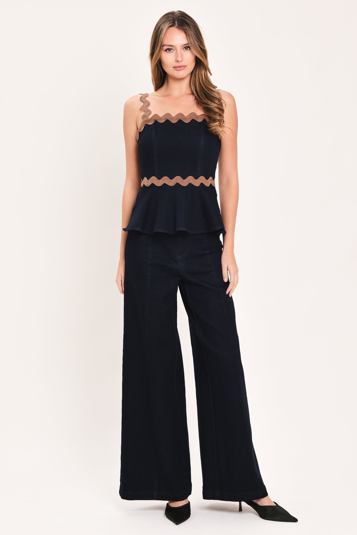 A woman wearing a navy blue sleeveless peplum top with brown wavy trim details | Flying Tomato