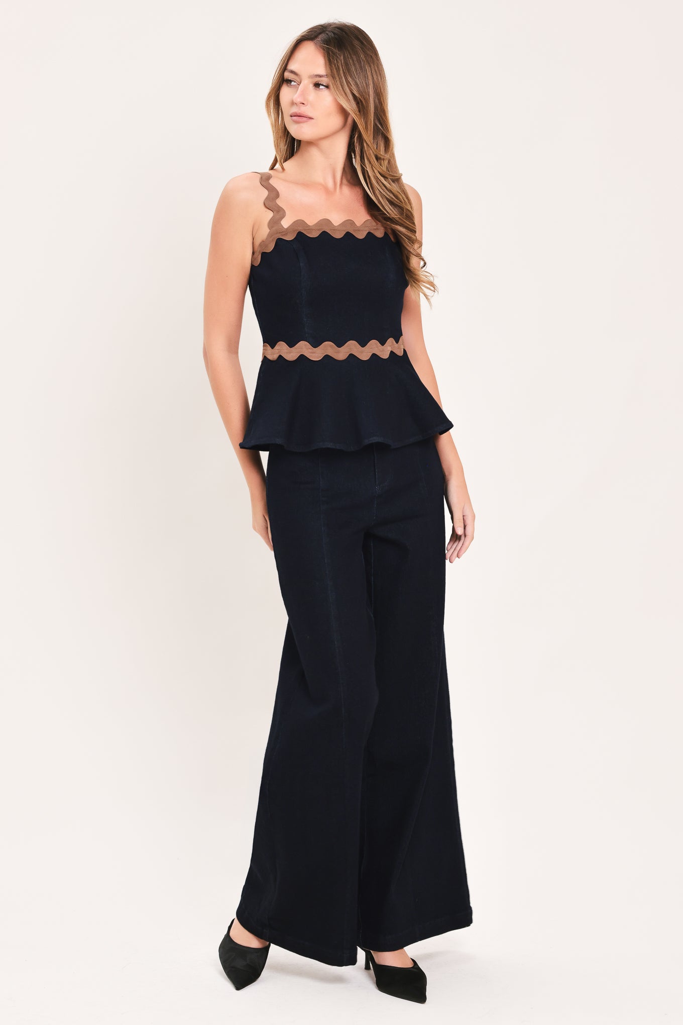 A woman wearing a navy blue sleeveless peplum top with brown wavy trim details | Flying Tomato