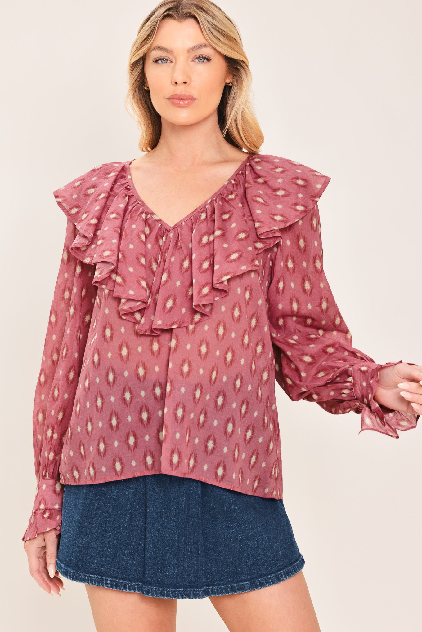 A woman wearing a dusty rose pink long-sleeve blouse with a white and beige ikat pattern, featuring layered ruffles around the V-neck and cuffs | Flying Tomato