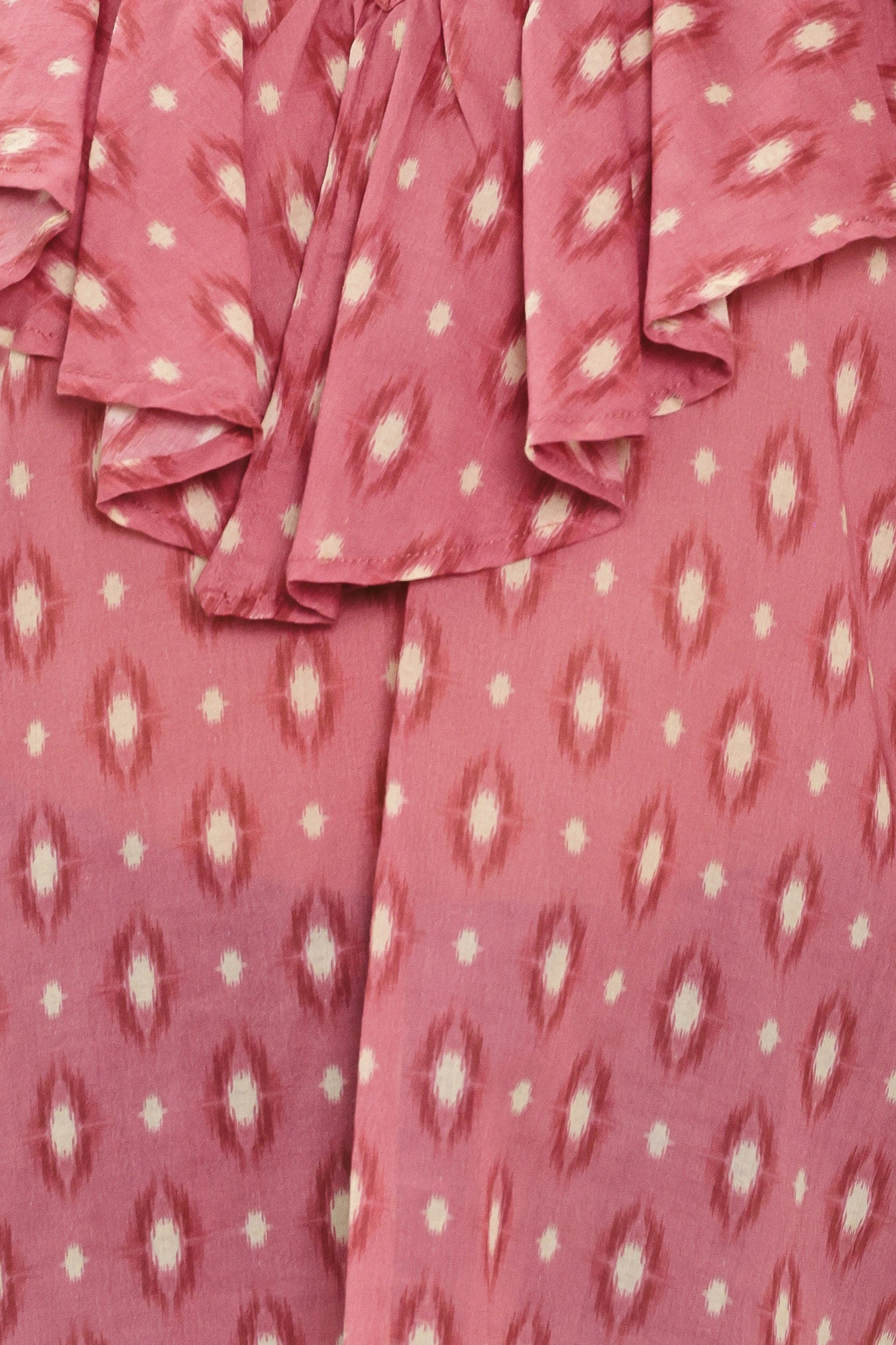 A woman wearing a dusty rose pink long-sleeve blouse with a white and beige ikat pattern, featuring layered ruffles around the V-neck and cuffs | Flying Tomato