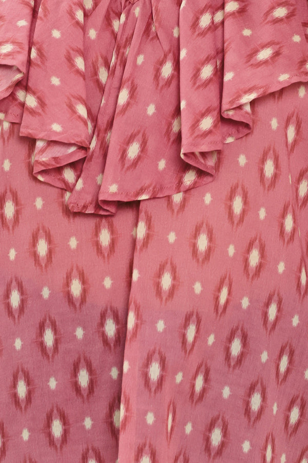 A woman wearing a dusty rose pink long-sleeve blouse with a white and beige ikat pattern, featuring layered ruffles around the V-neck and cuffs | Flying Tomato