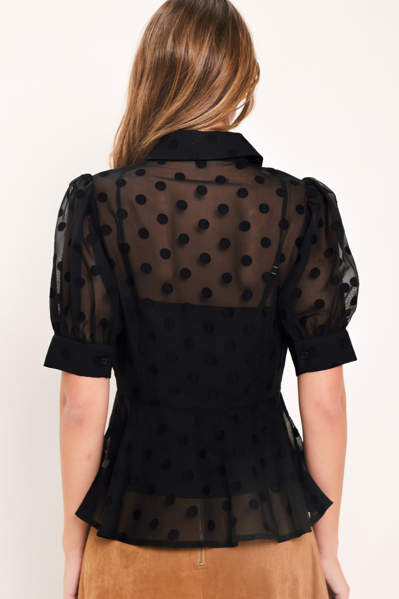 A woman wearing a black sheer puff-sleeve blouse with a subtle polka dot pattern and a peplum waist | Flying Tomato