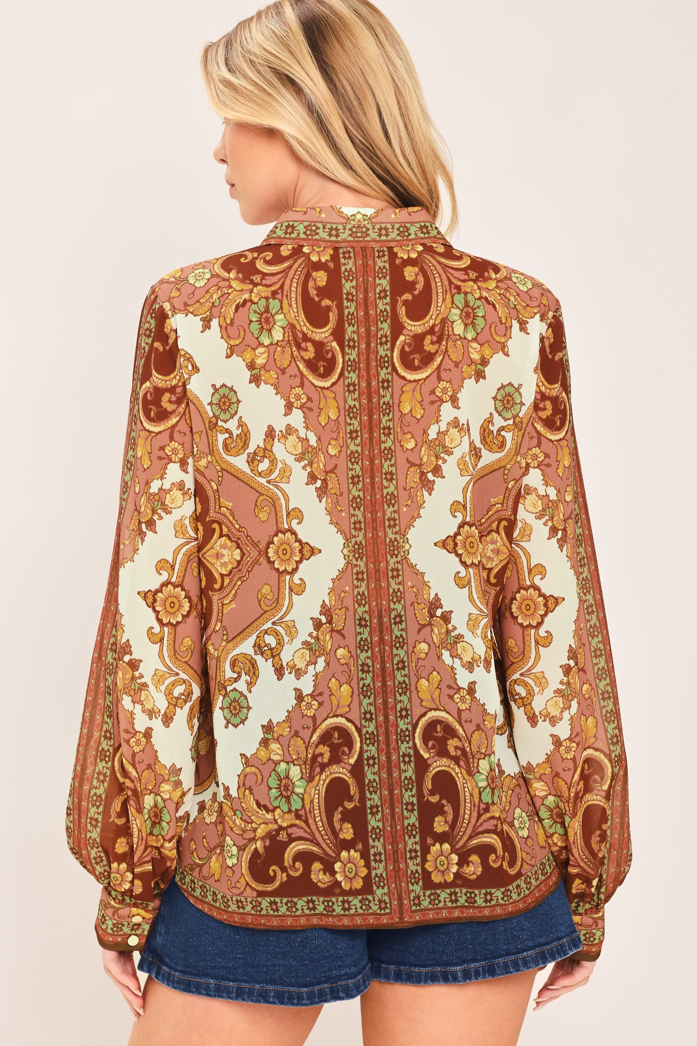 A woman wearing a long-sleeve button-up blouse with an ornate paisley and floral pattern in brown, gold, and cream | Flying Tomato