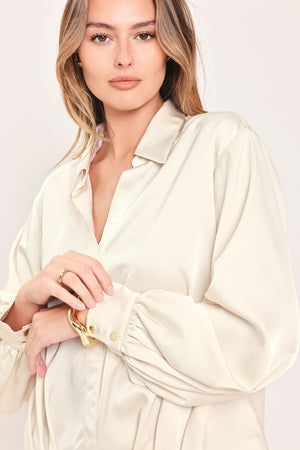 A woman wearing a champagne-colored satin long-sleeve blouse with a button-down front | Flying Tomato