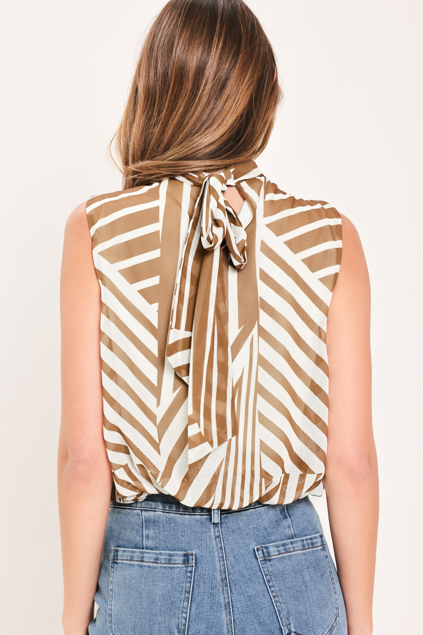 Woman wearing a sleeveless mocha and white geometric striped top with a high neck and flow silhouette | Flying Tomato