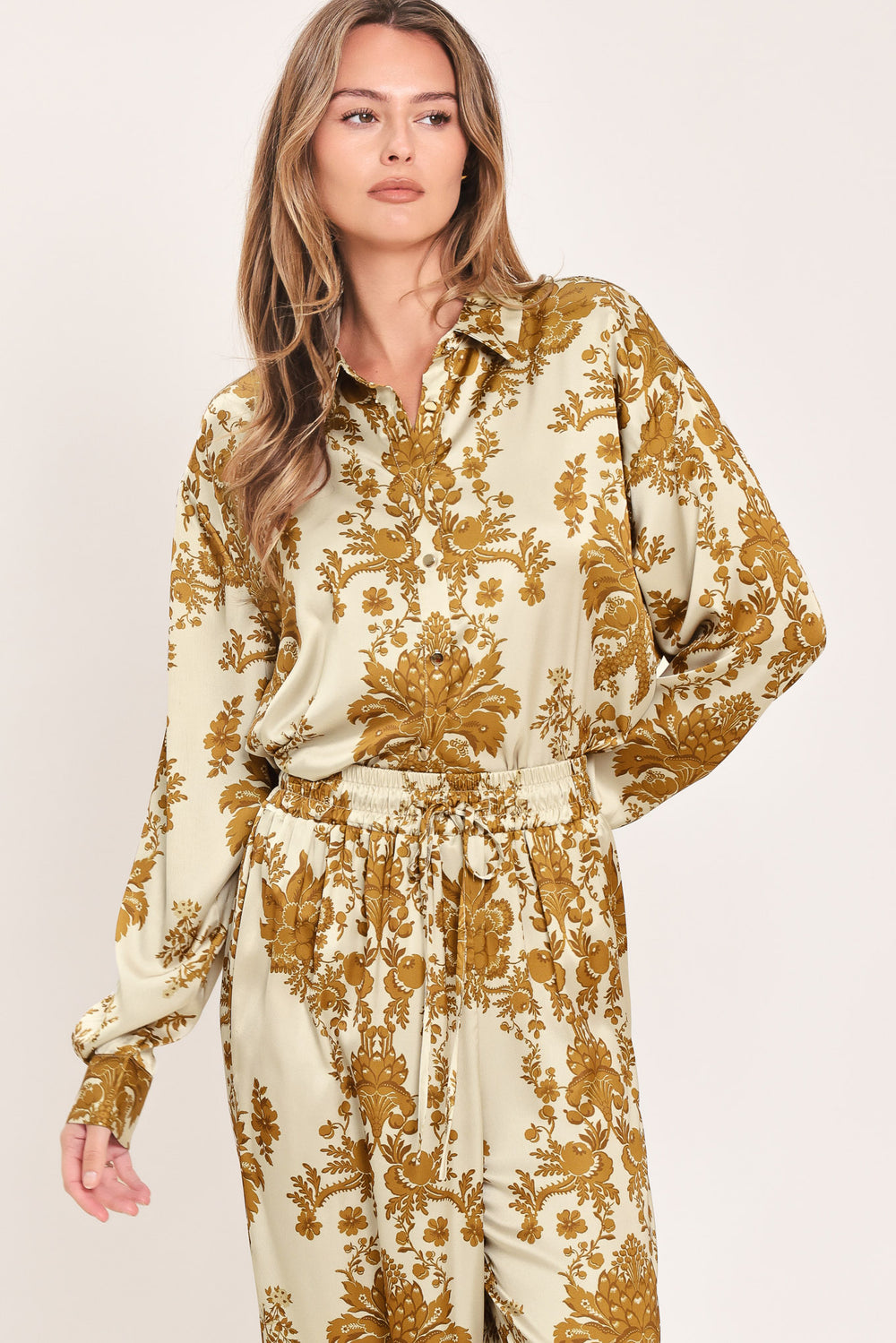 A woman wearing a long-sleeve button-up blouse with a beige and gold damask pattern | Flying Tomato