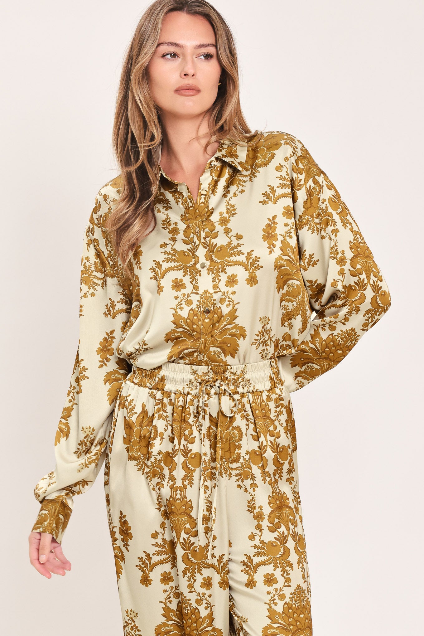 A woman wearing a long-sleeve button-up blouse with a beige and gold damask pattern | Flying Tomato
