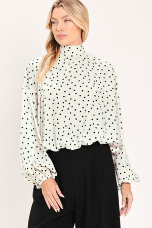 A woman wearing a white long-sleeve blouse with a black polka dot pattern and a high mock neck | Flying Tomato