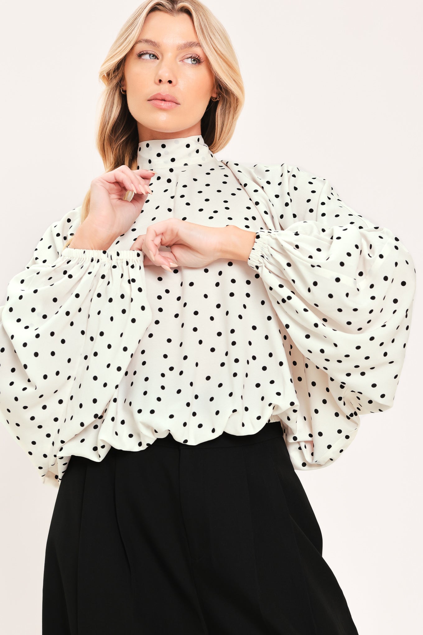 A woman wearing a white long-sleeve blouse with a black polka dot pattern and a high mock neck | Flying Tomato