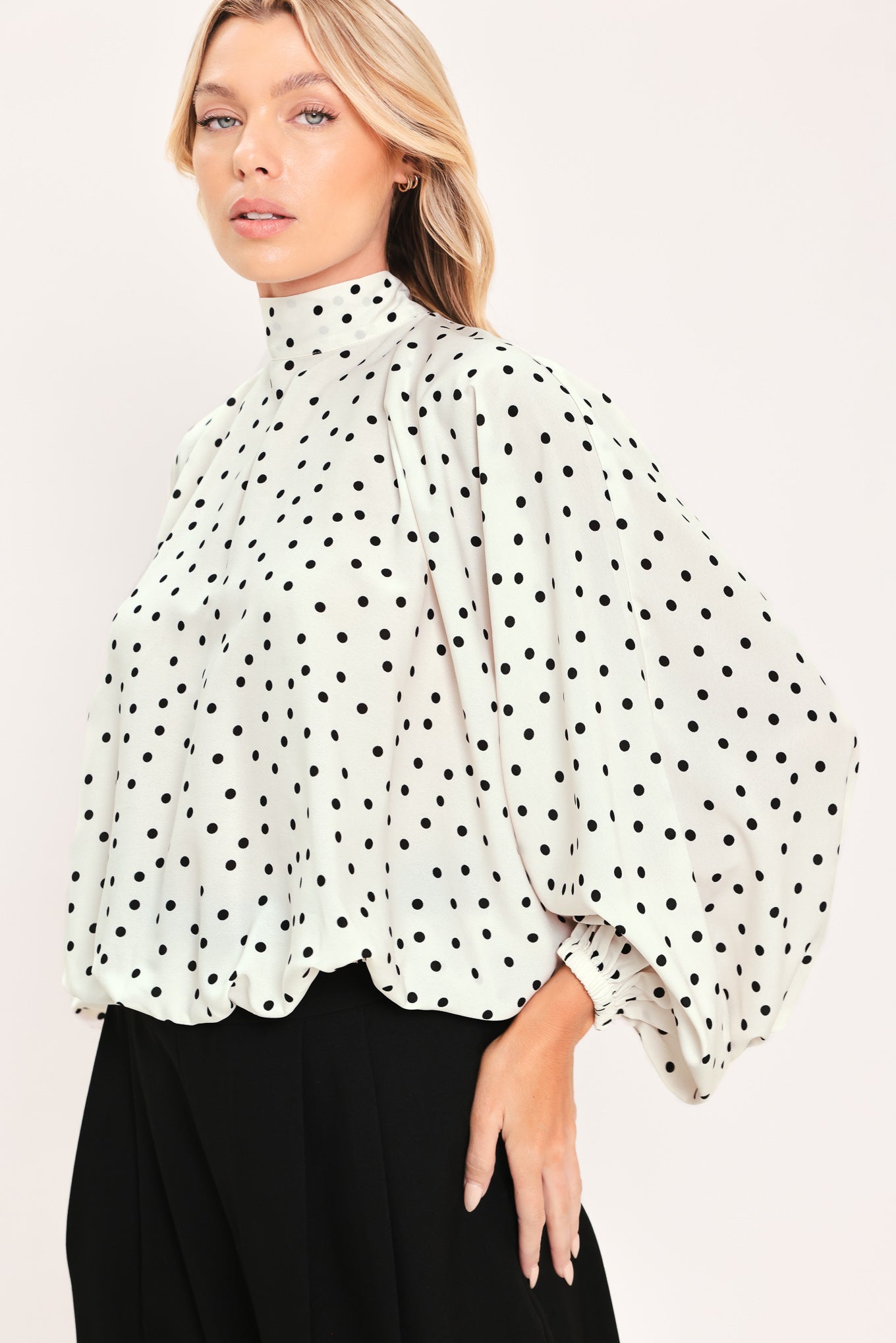 A woman wearing a white long-sleeve blouse with a black polka dot pattern and a high mock neck | Flying Tomato