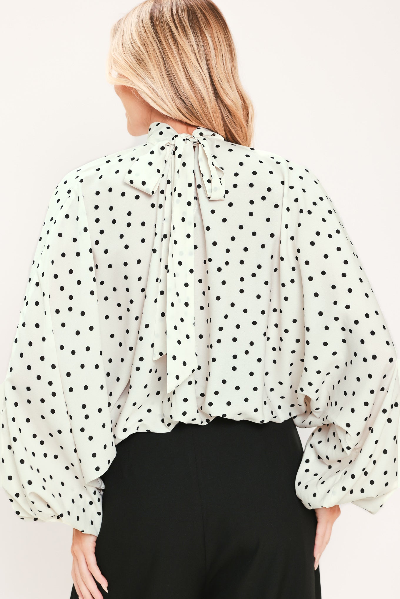 A woman wearing a white long-sleeve blouse with a black polka dot pattern and a high mock neck | Flying Tomato