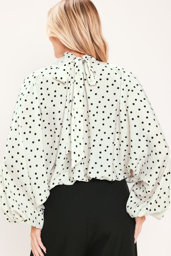 A woman wearing a white long-sleeve blouse with a black polka dot pattern and a high mock neck | Flying Tomato