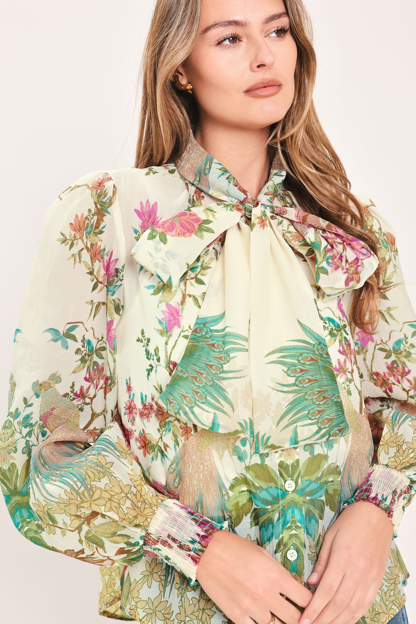 A woman wearing a long-sleeve blouse with a large bow at the collar and a tropical floral print | Flying Tomato
