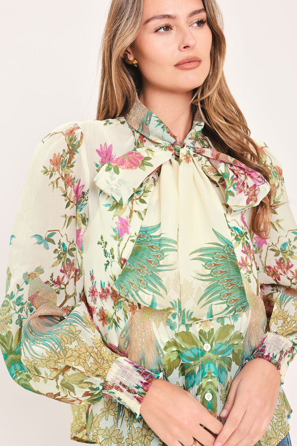 A woman wearing a long-sleeve blouse with a large bow at the collar and a tropical floral print | Flying Tomato