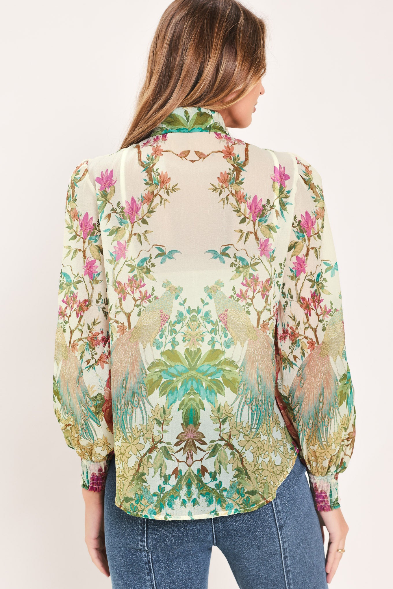 A woman wearing a long-sleeve blouse with a large bow at the collar and a tropical floral print | Flying Tomato