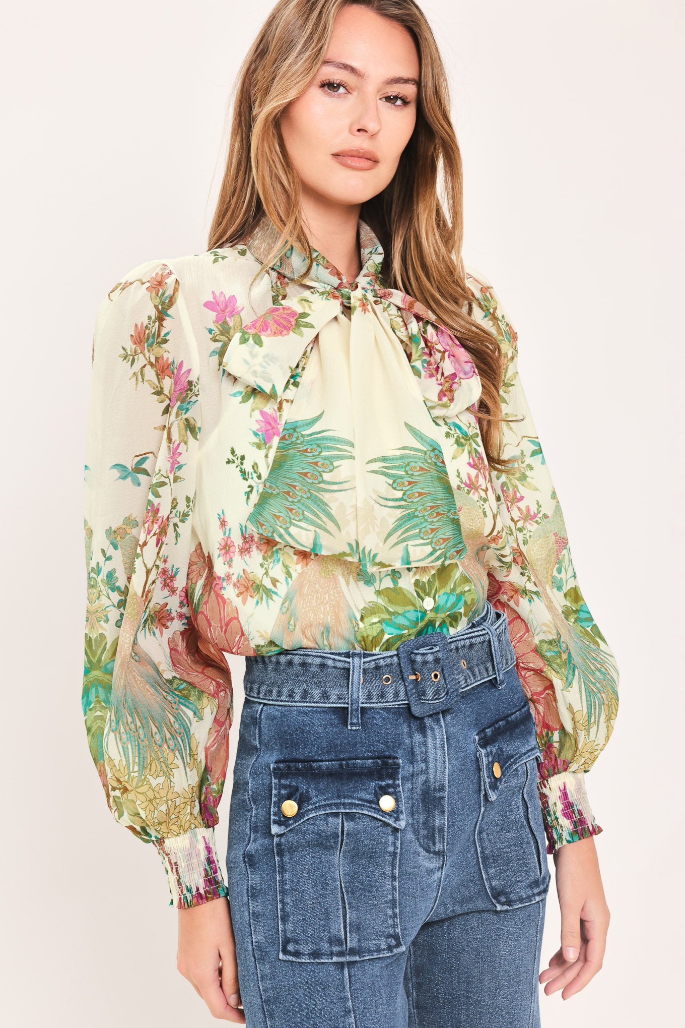 A woman wearing a long-sleeve blouse with a large bow at the collar and a tropical floral print | Flying Tomato
