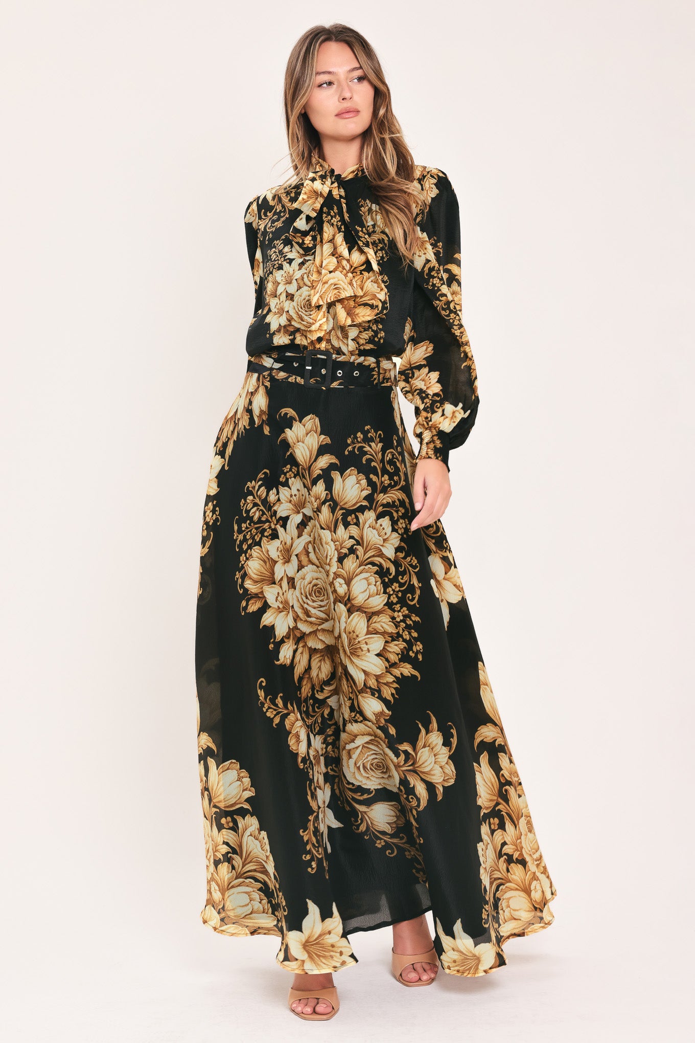 A woman wearing a black long-sleeve blouse with a large beige and gold floral print, featuring a high neck and bow detail | Flying Tomato