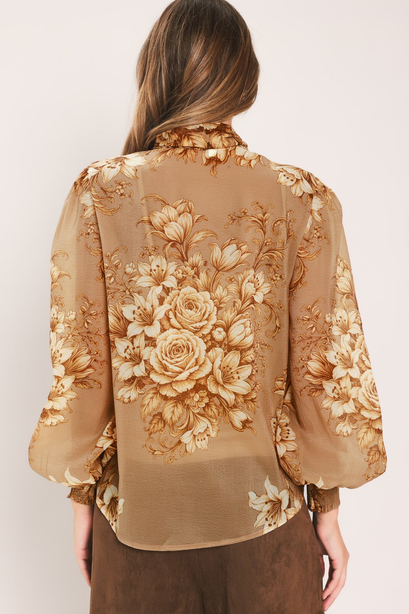 A woman wearing a sheer beige blouse with a large gold floral print and a bow tie neckline | Flying Tomato