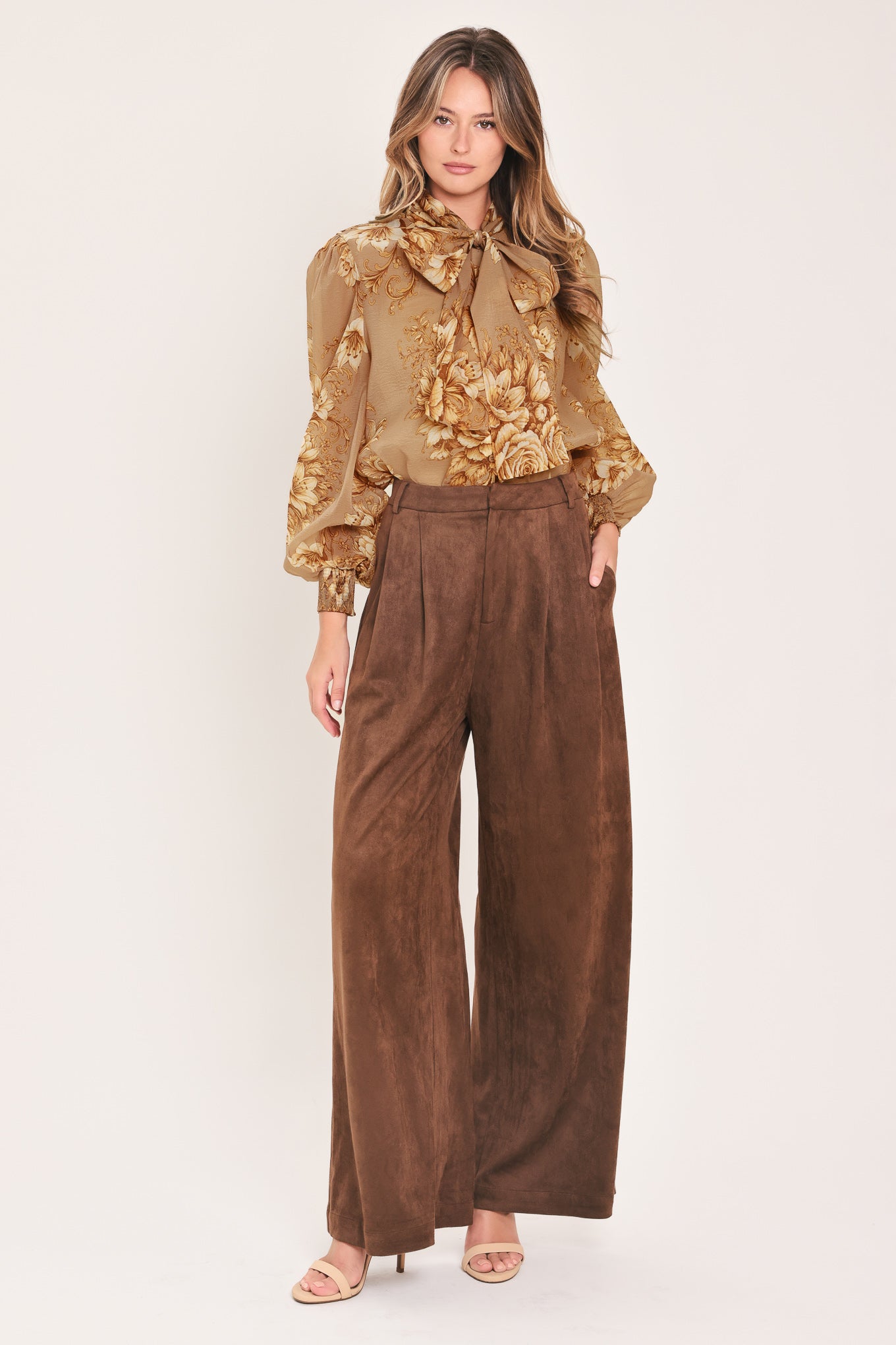 A woman wearing a sheer beige blouse with a large gold floral print and a bow tie neckline | Flying Tomato