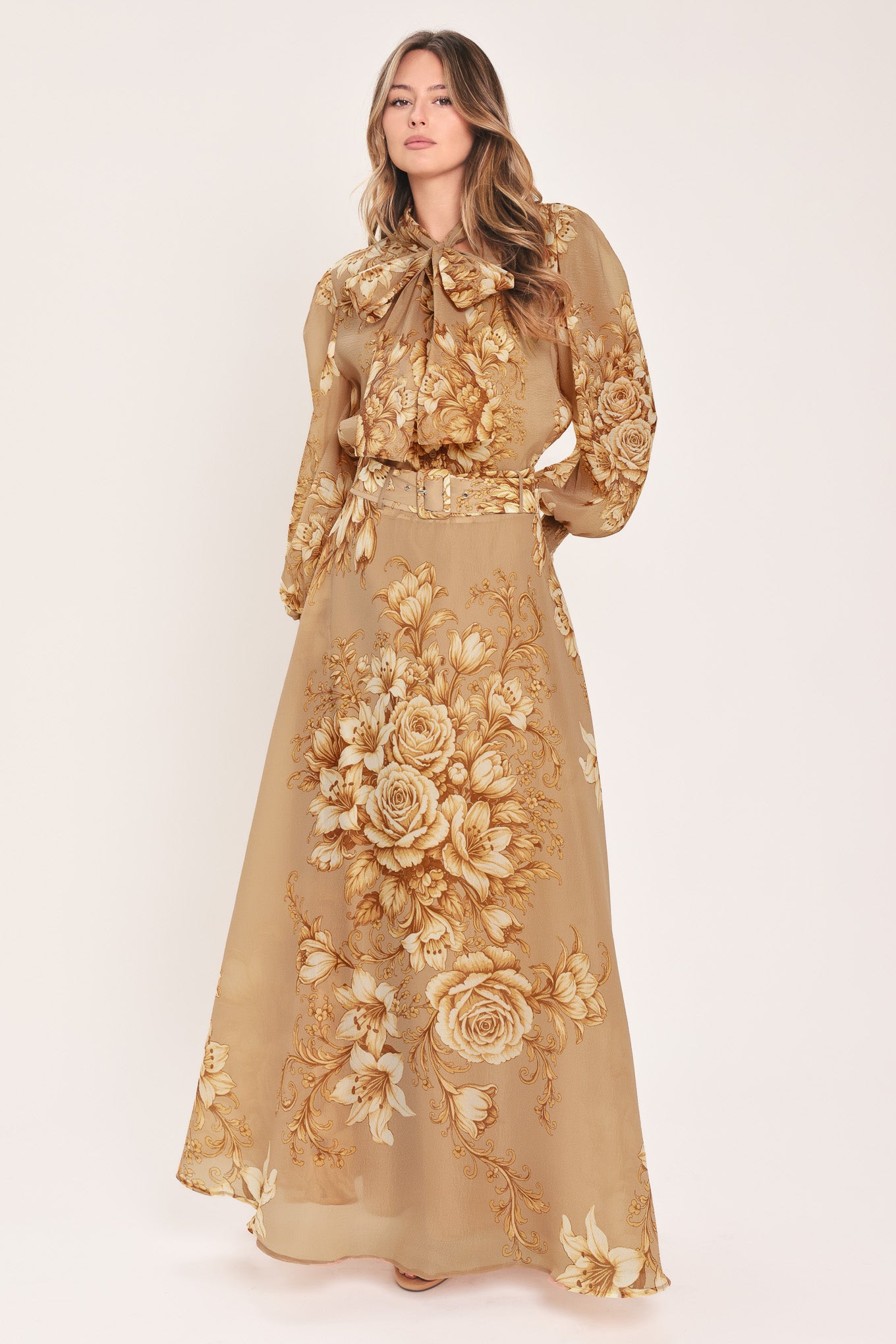A woman wearing a sheer beige blouse with a large gold floral print and a bow tie neckline | Flying Tomato