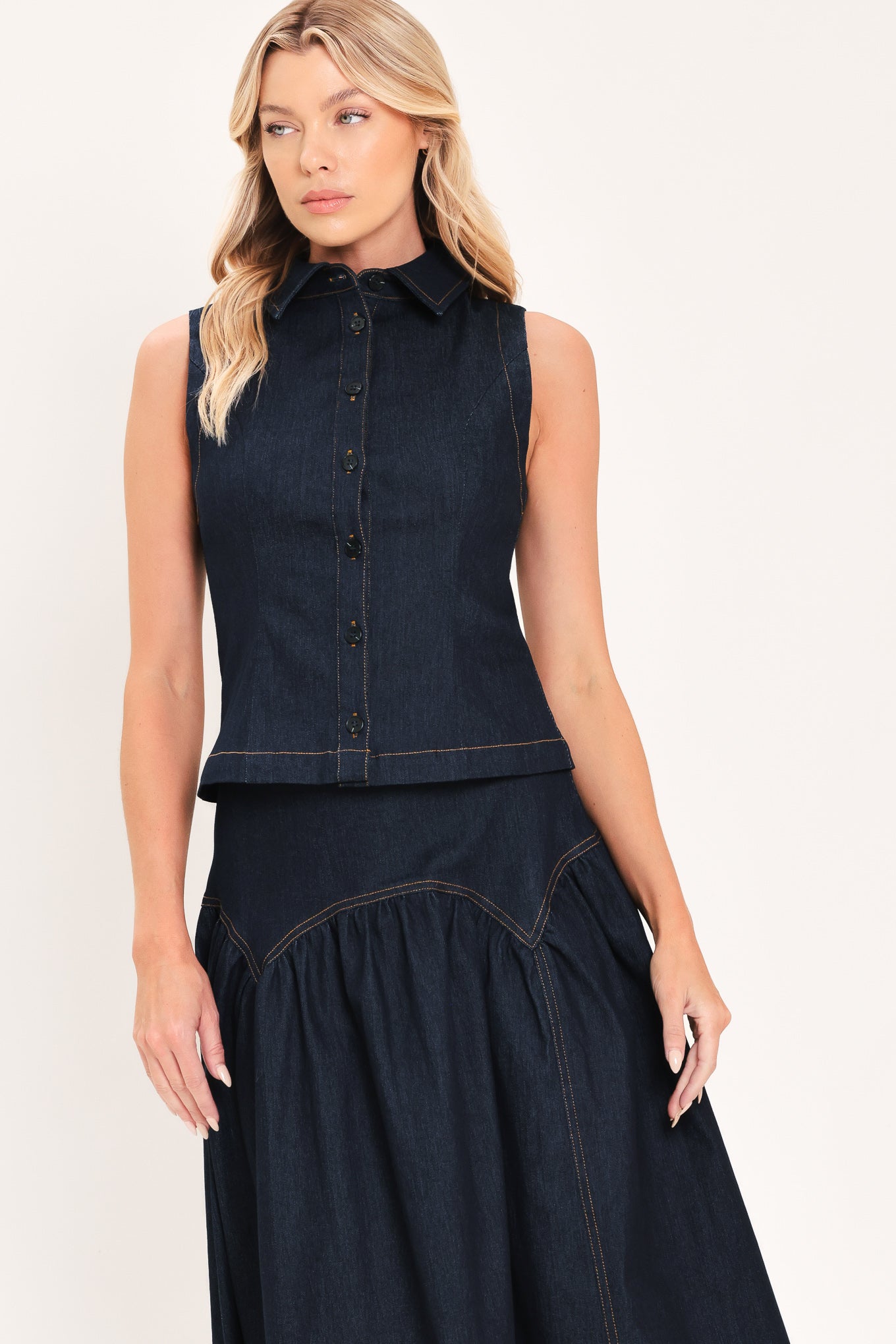A woman modeling a sleeveless dark denim top and midi skirt  with a button-front bodice, pointed collar, and a gathered skirt | Flying Tomato