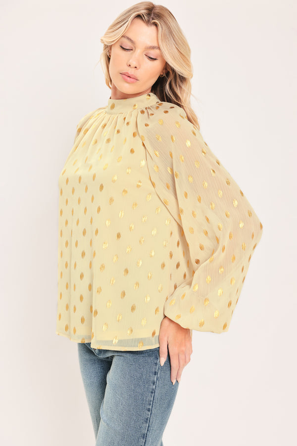 A woman wearing a light beige high-neck blouse with metallic gold polka dots and voluminous long sleeves | Flying Tomato
