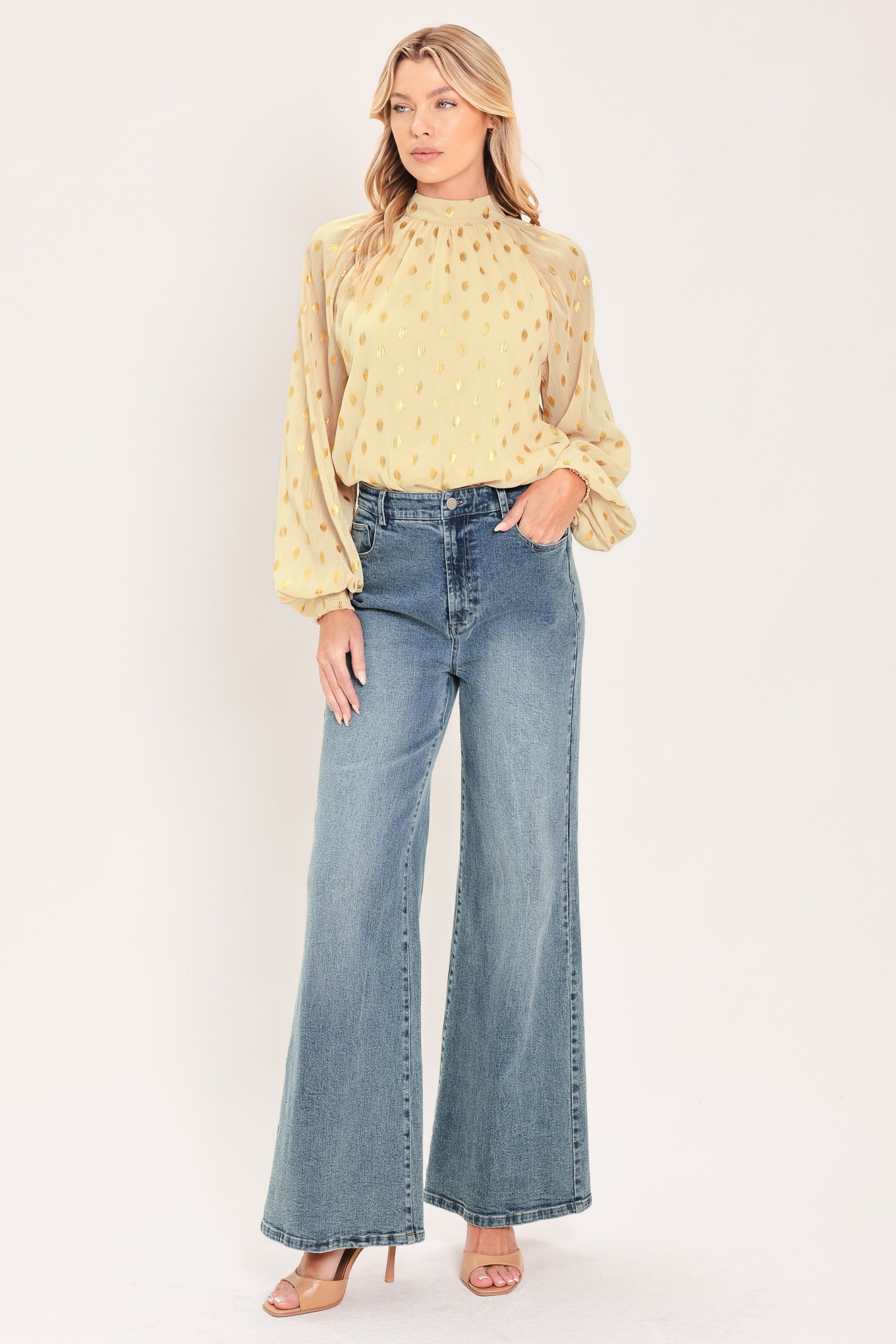 A woman wearing a light beige high-neck blouse with metallic gold polka dots and voluminous long sleeves | Flying Tomato