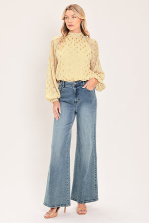 A woman wearing a light beige high-neck blouse with metallic gold polka dots and voluminous long sleeves | Flying Tomato