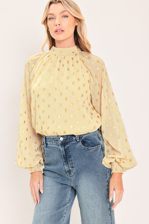 A woman wearing a light beige high-neck blouse with metallic gold polka dots and voluminous long sleeves | Flying Tomato