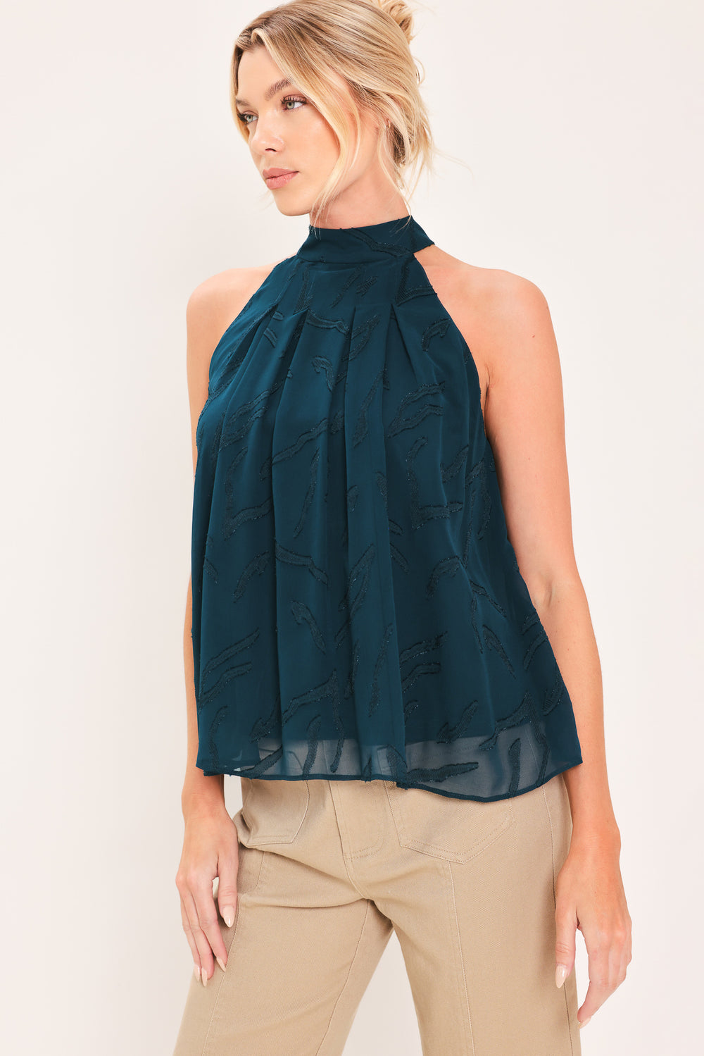A woman wearing a sleeveless high-neck halter top in dark teal with a subtle tonal pattern | Flying Tomato