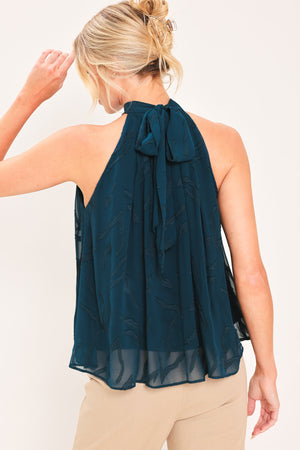 A woman wearing a sleeveless high-neck halter top in dark teal with a subtle tonal pattern | Flying Tomato