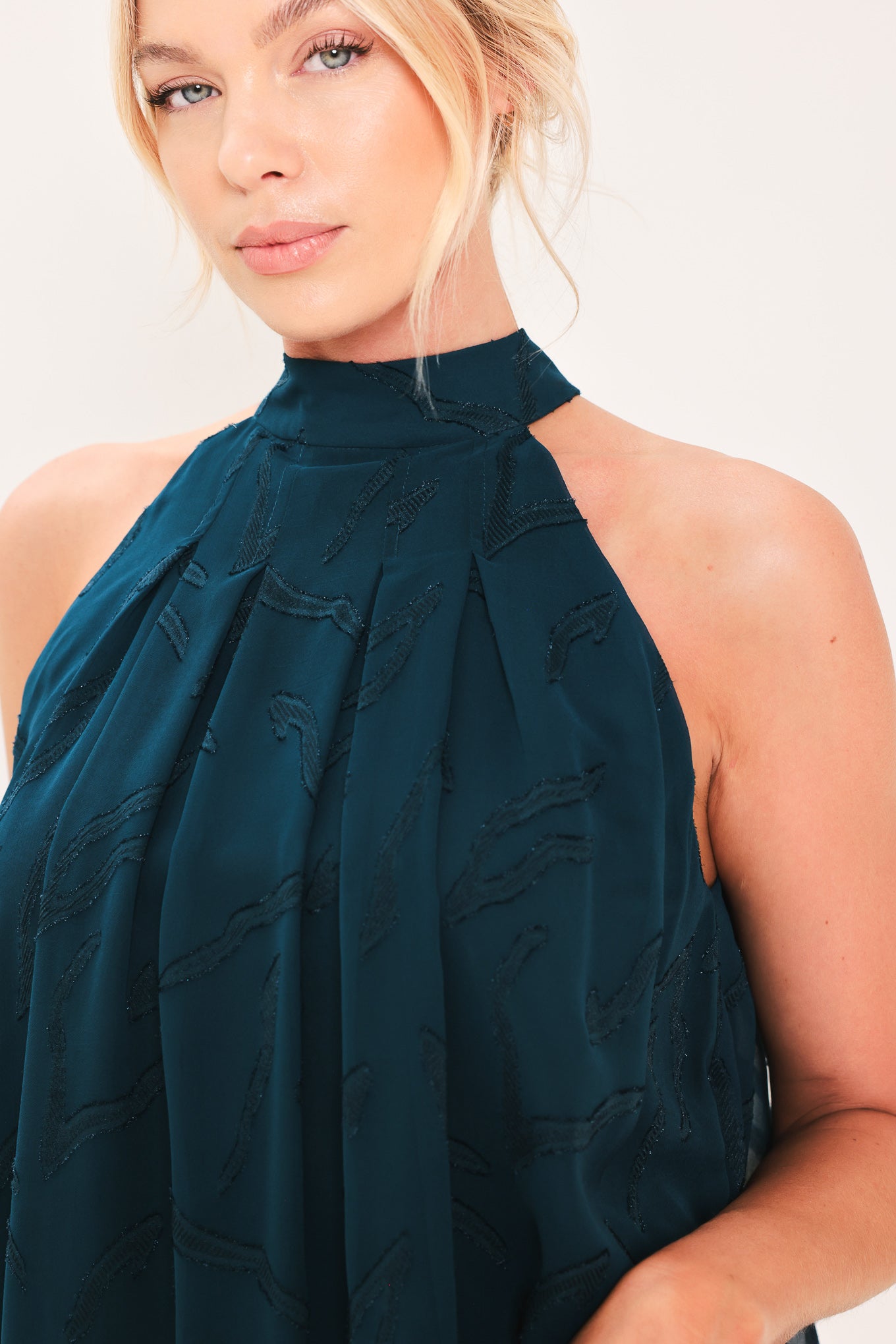 A woman wearing a sleeveless high-neck halter top in dark teal with a subtle tonal pattern | Flying Tomato