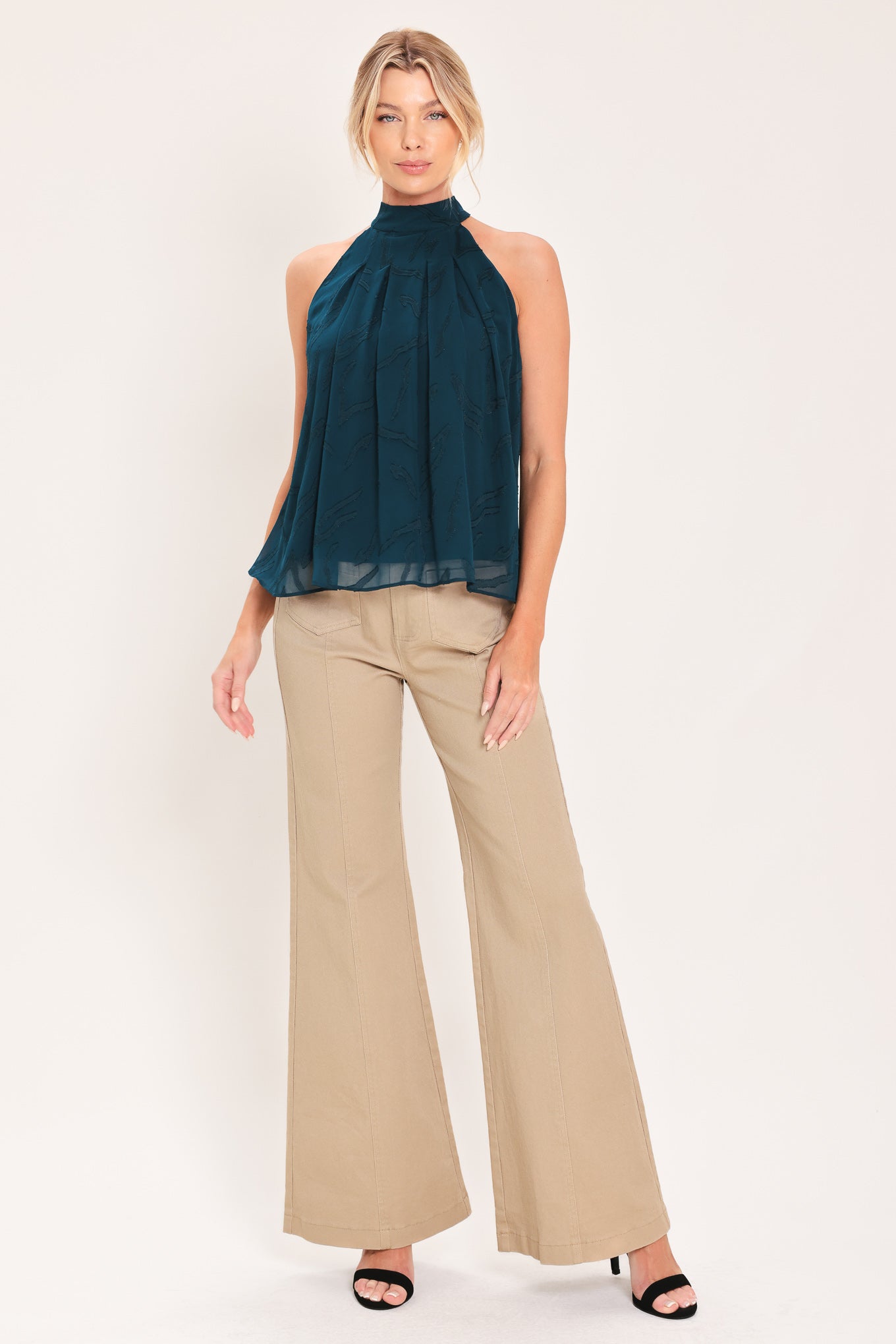 A woman wearing a sleeveless high-neck halter top in dark teal with a subtle tonal pattern | Flying Tomato