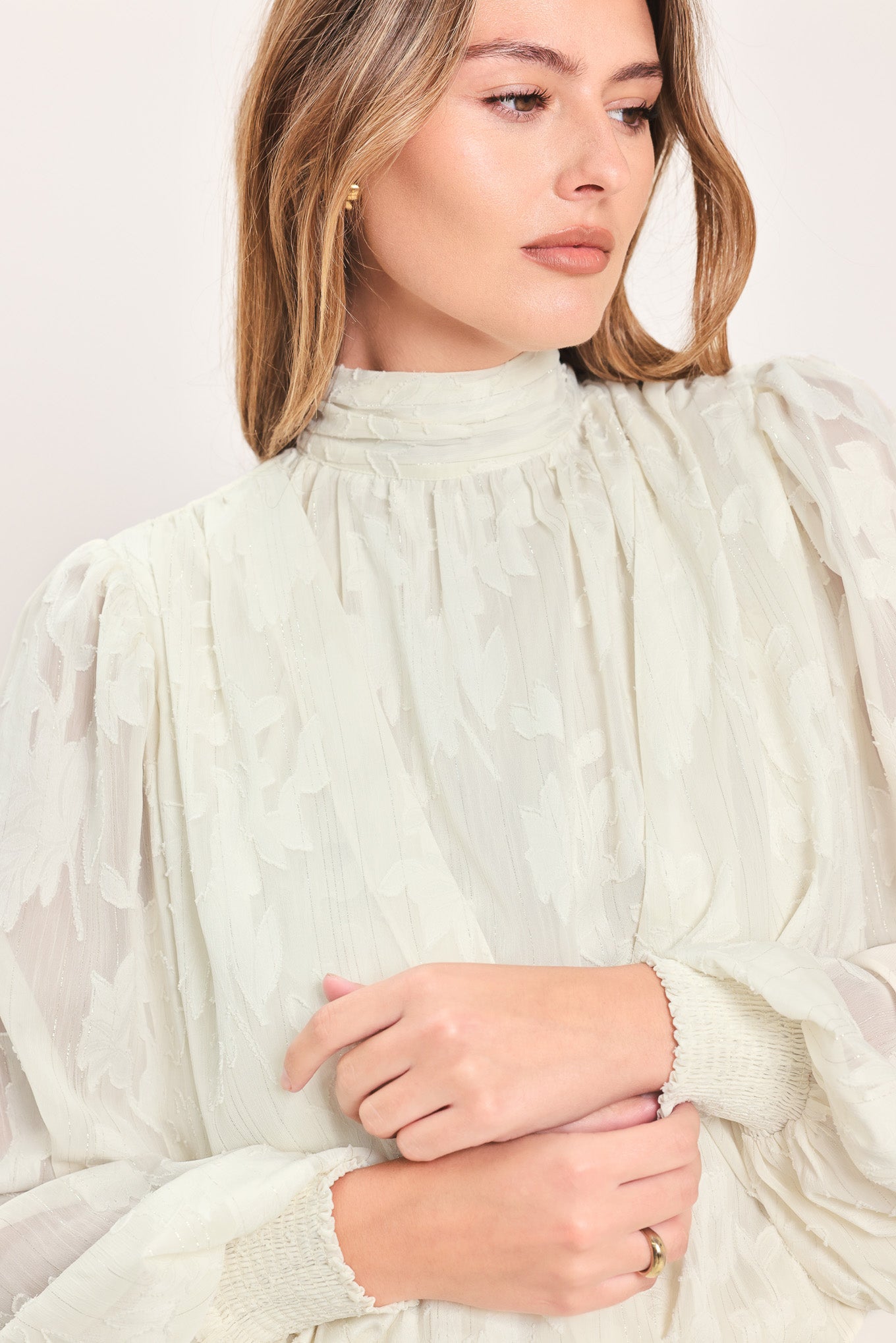 A woman wearing a cream-colored, semi-sheer long-sleeve blouse with a high neck | Flying Tomato