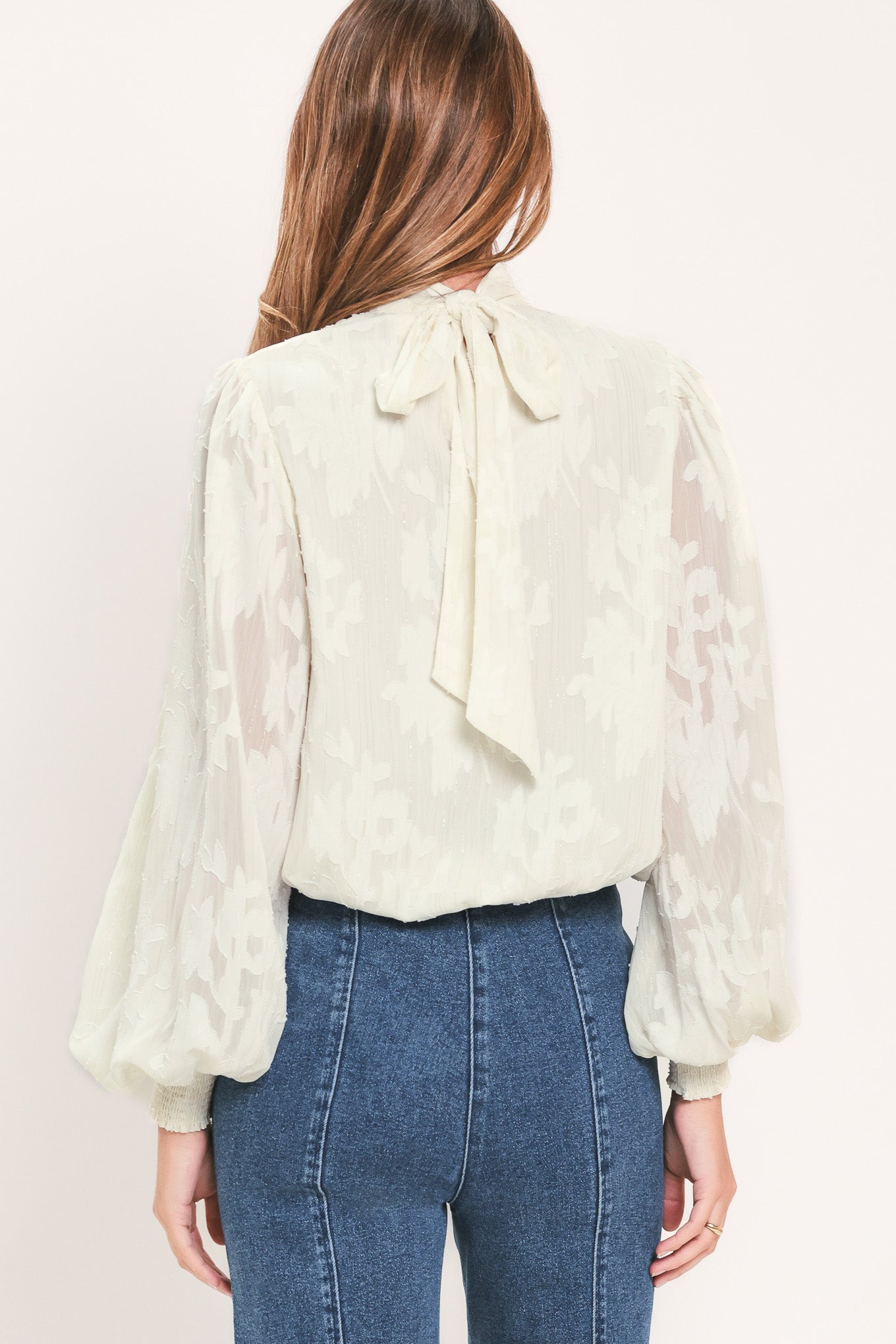 A woman wearing a cream-colored, semi-sheer long-sleeve blouse with a high neck | Flying Tomato