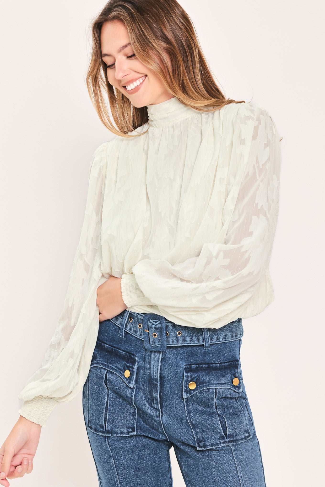 A woman wearing a cream-colored, semi-sheer long-sleeve blouse with a high neck | Flying Tomato