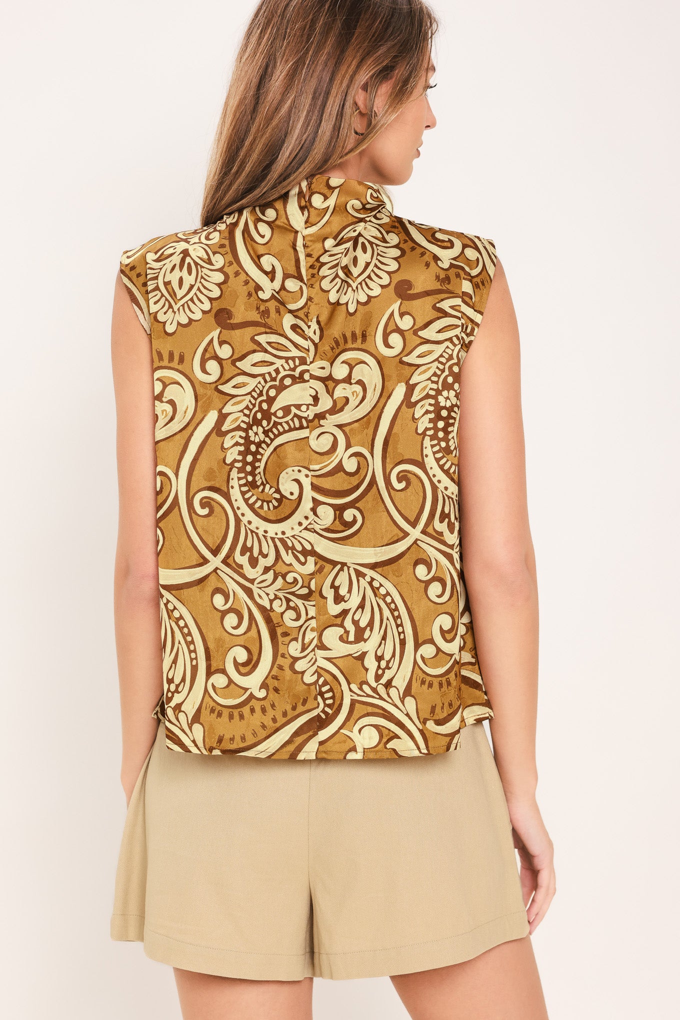 Woman wearing a sleeveless brown multi-toned printed woven top with funnel neckline and back zipper closure | Flying Tomato