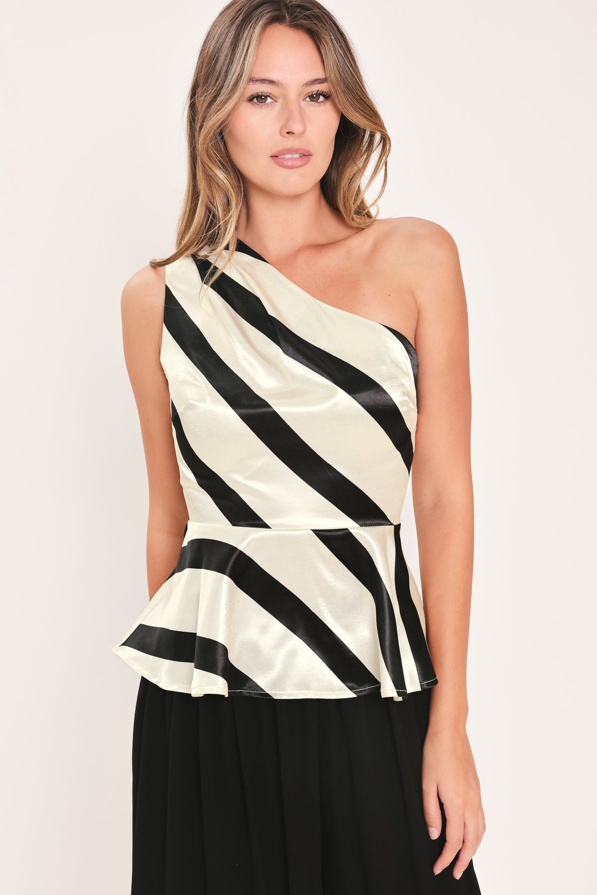 A woman modeling a sleeveless one-shoulder peplum top with diagonal black and cream satin-like stripes | Flying Tomato
