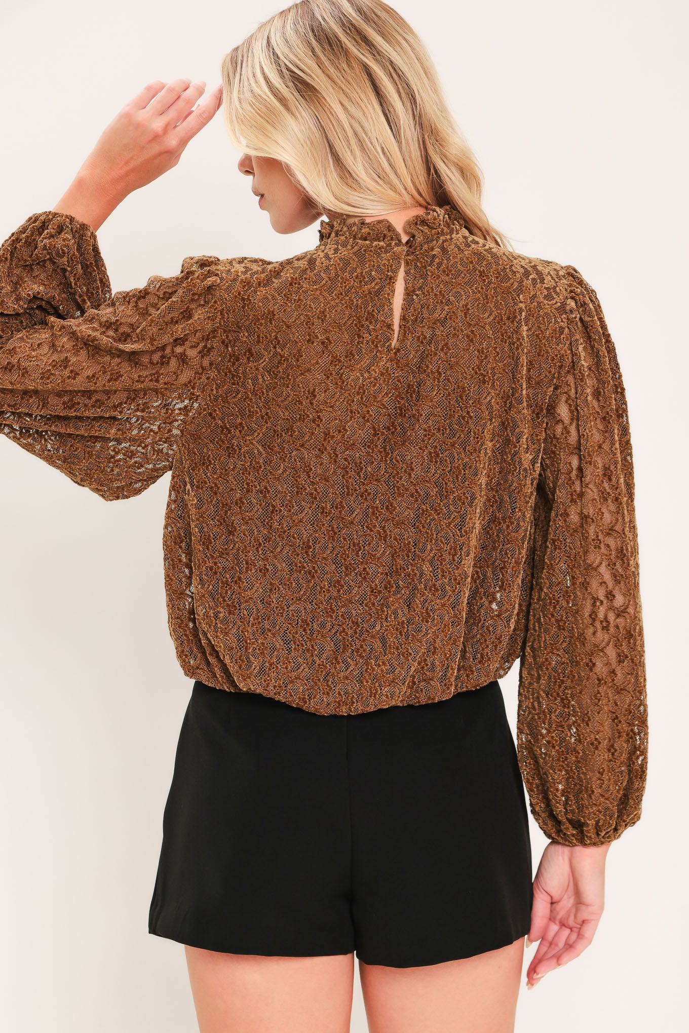 A woman modeling a brown textured long-sleeve top with a ruffled mock neck and embellishments around the neckline | Flying Tomato