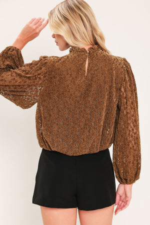 A woman modeling a brown textured long-sleeve top with a ruffled mock neck and embellishments around the neckline | Flying Tomato
