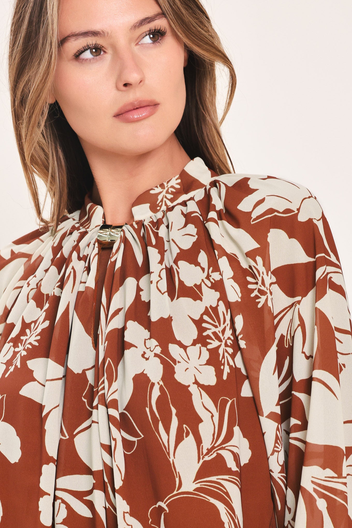A woman wearing a rust-brown and cream floral print blouse with long sheer sleeves and a tie-neck detail | Flying Tomato