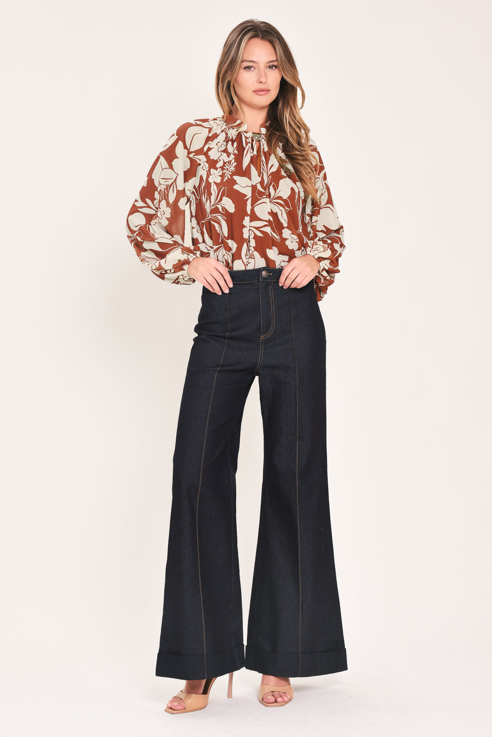 A woman wearing a rust-brown and cream floral print blouse with long sheer sleeves and a tie-neck detail | Flying Tomato