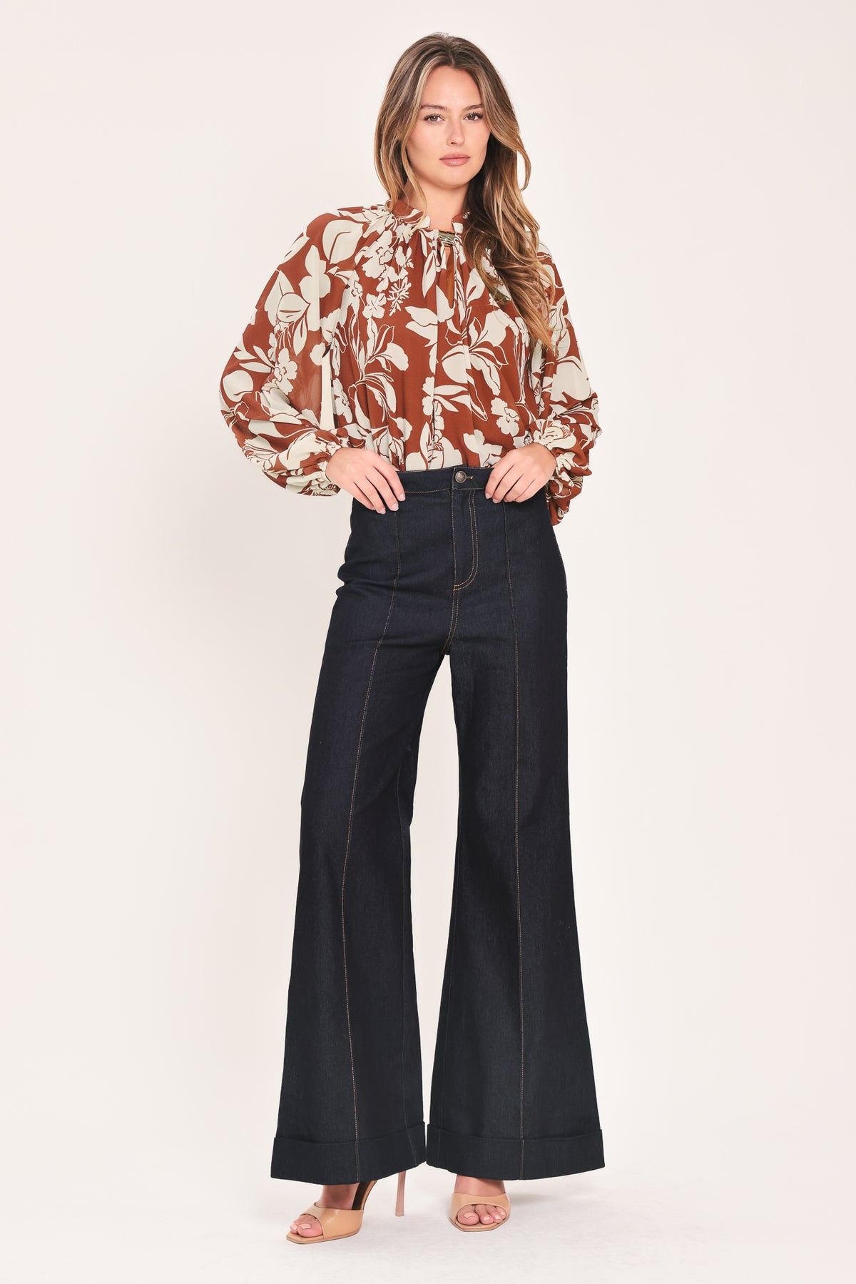 A woman wearing a rust-brown and cream floral print blouse with long sheer sleeves and a tie-neck detail | Flying Tomato