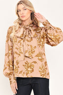 Woman wearing a long sleeve mauve top with a beige floral print and bow around the neck | Flying Tomato