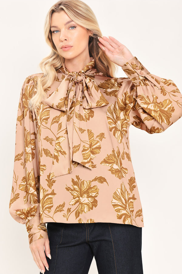 Woman wearing a long sleeve mauve top with a beige floral print and bow around the neck | Flying Tomato