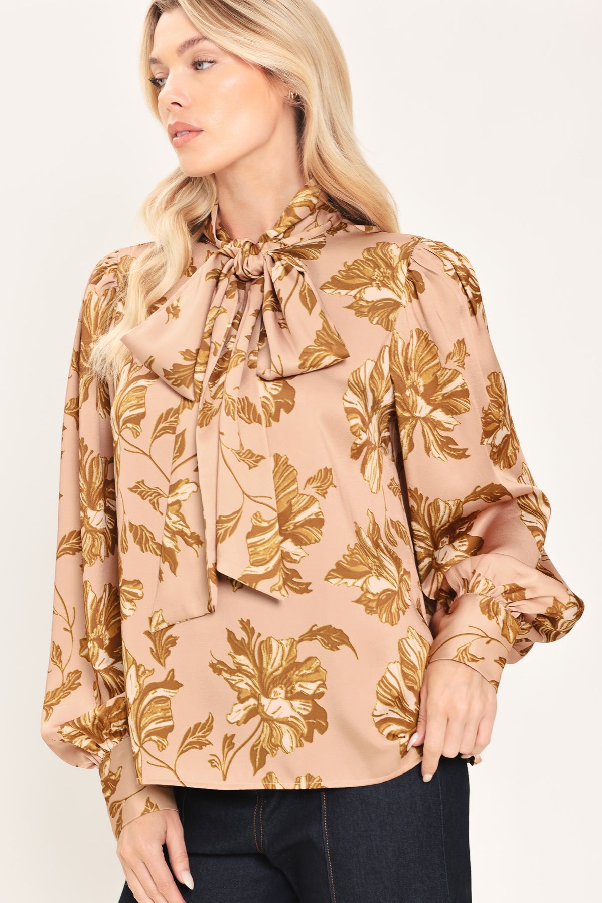 Woman wearing a long sleeve mauve top with a beige floral print and bow around the neck | Flying Tomato
