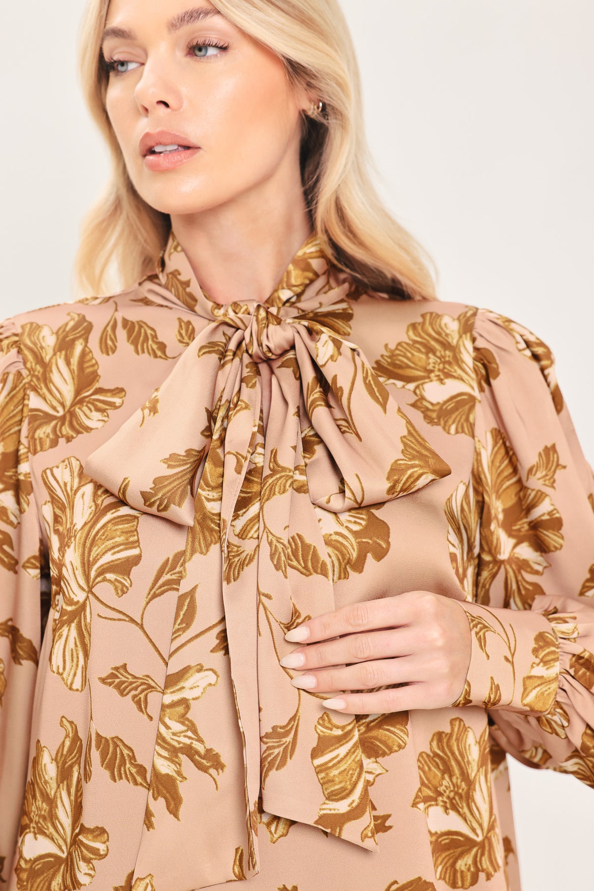 Woman wearing a long sleeve mauve top with a beige floral print and bow around the neck | Flying Tomato