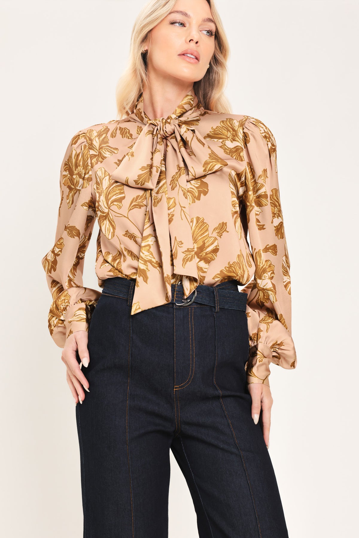 Woman wearing a long sleeve mauve top with a beige floral print and bow around the neck | Flying Tomato